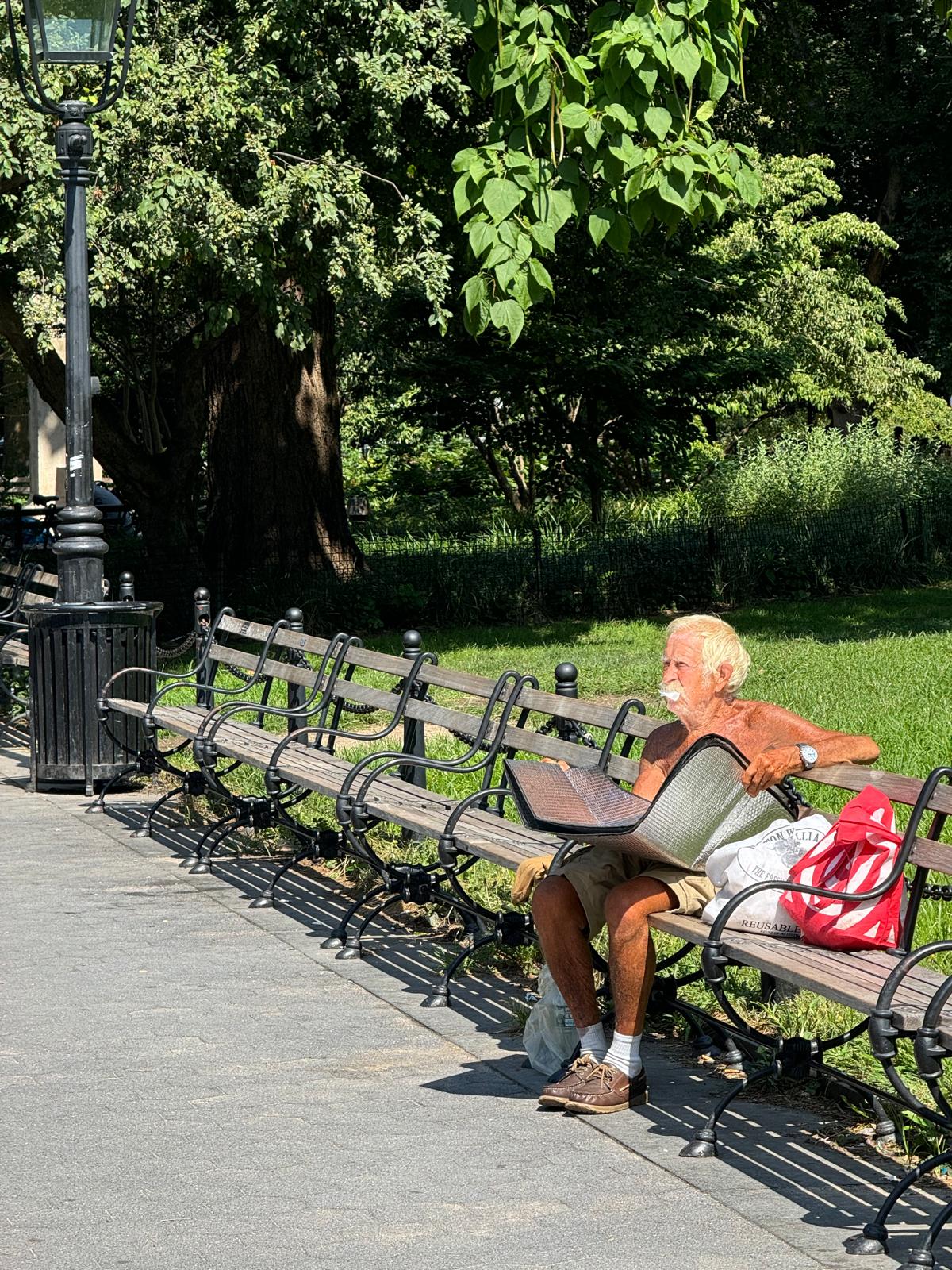 Old man sunbathing with mirrors on a park bench